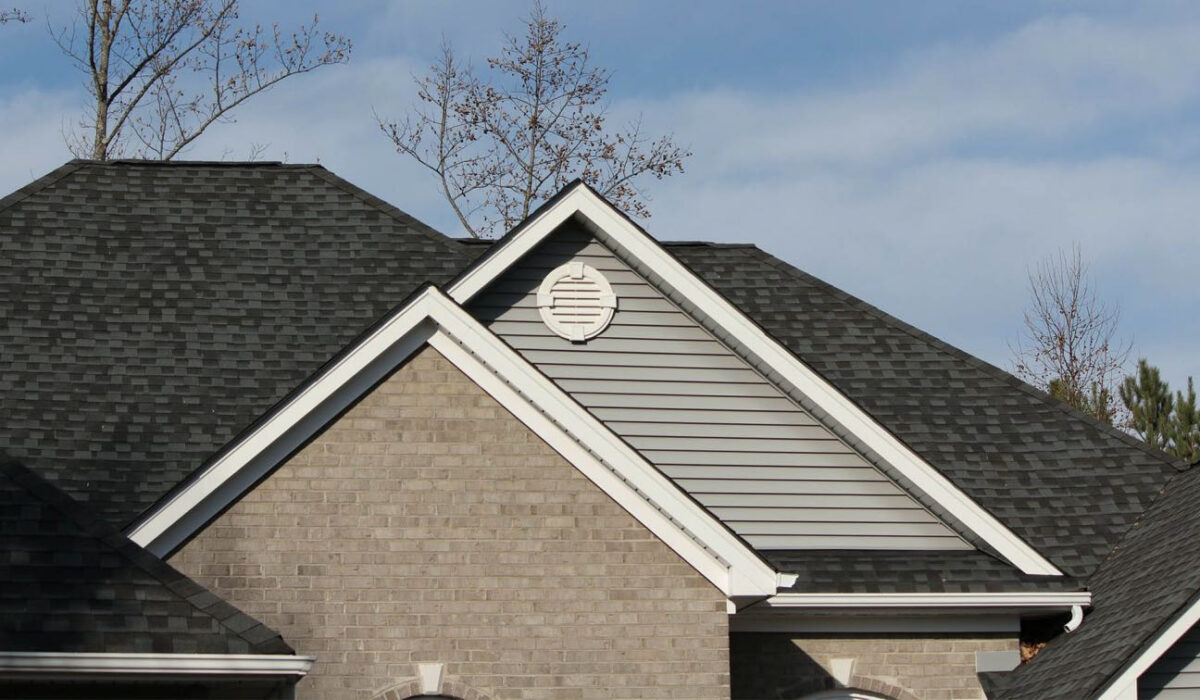 up of a residential roof with dark asphalt shingles, grey horizontal siding on a gable end, and white trim, illustrating potential areas where sagging might become visible.