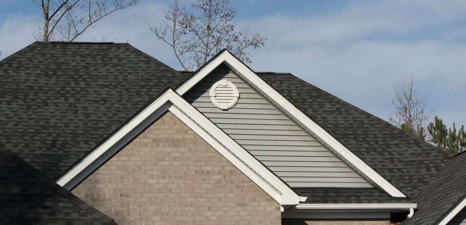 up of a residential roof with dark asphalt shingles, grey horizontal siding on a gable end, and white trim, illustrating potential areas where sagging might become visible.